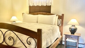 A wooden bed with a headboard, two bedside tables with lamps, and a window with a lace curtain.