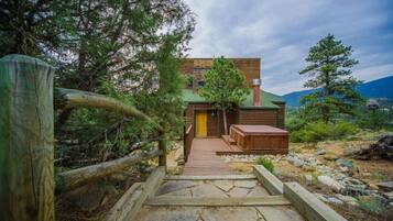 A wooden cabin with a stone pathway leading to a wooden deck and a small wooden structure.