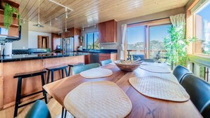 A modern kitchen with wooden cabinets, a central island, and a dining area with a wooden table and chairs. - Best Views, Hot Tub Near National Park! King Beds! (Estes Park)