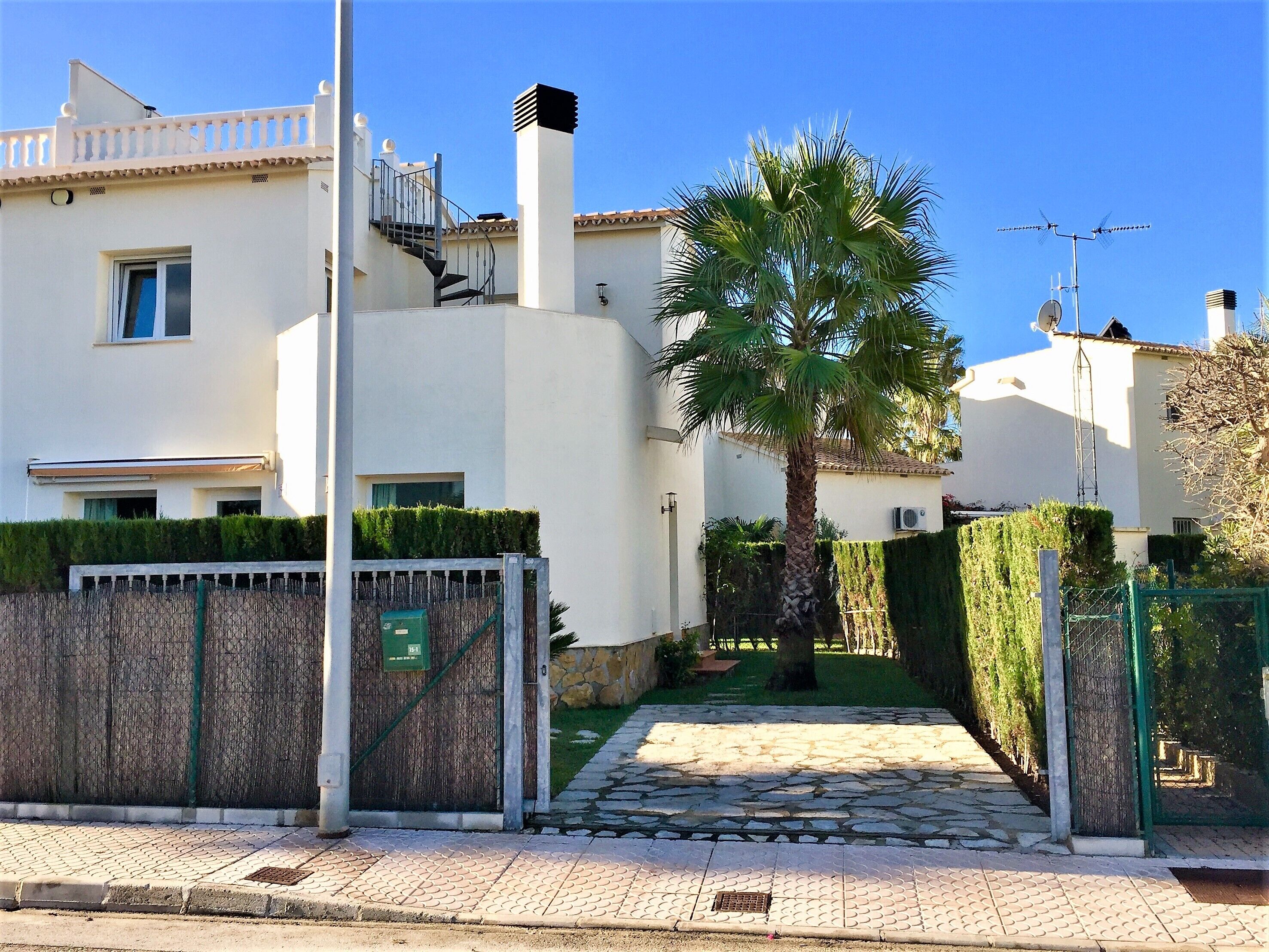 A white building with a gated entrance, a palm tree, and a stone pathway leading to the door.