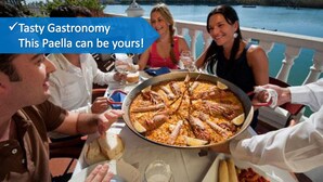 A paella dish on a table with people around it.