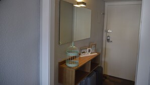 A small bathroom with a wooden shelf, a mirror, a birdcage, and a door.