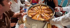 A paella dish on a table with people around it.