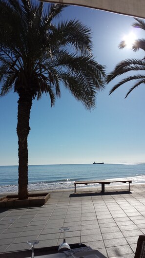 Eine Sitzgelegenheit am Strand mit einer Palme, einer Bank und Blick aufs Meer.