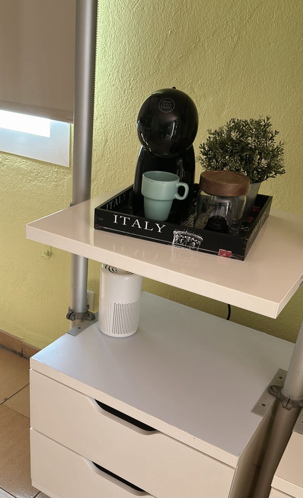 Una cafetera sobre un estante con una taza y una planta pequeña.