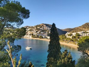 A coastal town with buildings on a hillside, a clear blue sea, and a boat. - Cozy seaview studio with 2 terraces 5m from the beach - Casa ArteVida (Roses)