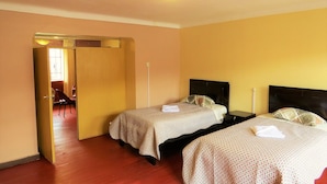 Een hotelkamer met twee bedden, een houten vloer en een deur naar een gang.