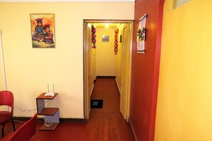 A hallway with a red chair, a small desk with a computer, and a painting on the wall.
