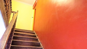 Een trap met houten treden en een leuning, leidend naar een kamer met een gele muur en een rode deur.