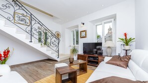 A modern living room with a staircase, white sofas, a flat-screen TV, and a wooden coffee table.