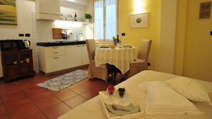 A compact hotel room with a kitchenette, a dining area with a table and chairs, and a bed with neatly made linens. - THE HIDDEN GARDEN (Bologna)