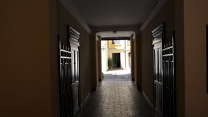 A narrow hallway with a brick floor and beige walls, leading to a courtyard with a gate. - THE HIDDEN GARDEN (Bologna)