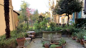 A courtyard with potted plants, a wooden chair, and a table. - THE HIDDEN GARDEN (Bologna)