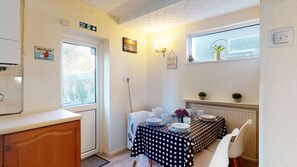 A small kitchen with a dining table set for two, a window with a view of trees, and a fire exit sign.