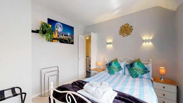A bedroom with a bed, bedside tables, a nightstand, a wheelchair, a wall-mounted lamp, and a painting of a cityscape. - Orchard in Orpington (St Paul's Cray, Orpington) (Orpington)