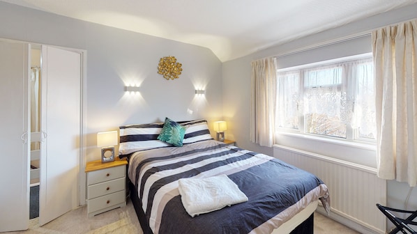 A bedroom with a bed, bedside lamps, a wall-mounted light fixture, a window with curtains, and a wardrobe.