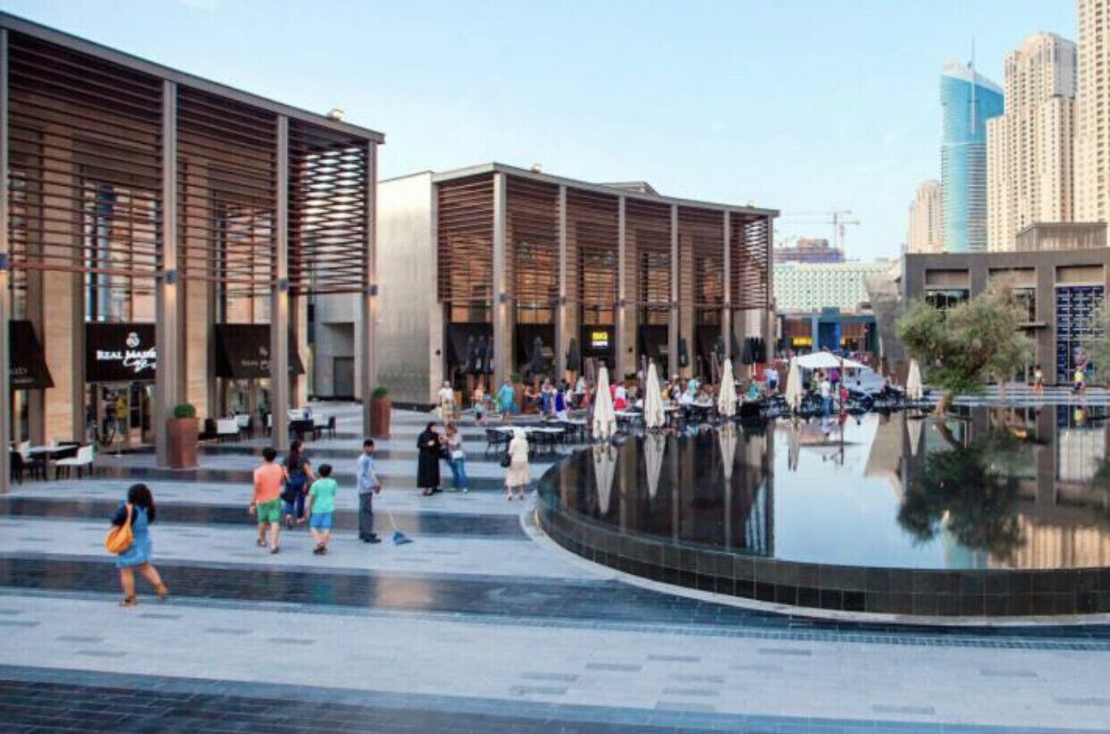 A public square with a fountain, modern buildings, and outdoor seating areas.