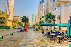 A city street with outdoor seating, palm trees, and tall buildings.