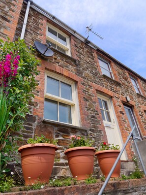 Une maison en briques avec trois jardinières en terre cuite sur les marches de l’entrée, une antenne parabolique et une porte dotée d’une petite fenêtre.