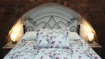 A bed with a floral-patterned duvet and pillows, flanked by two bedside lamps, set against a brick wall backdrop.