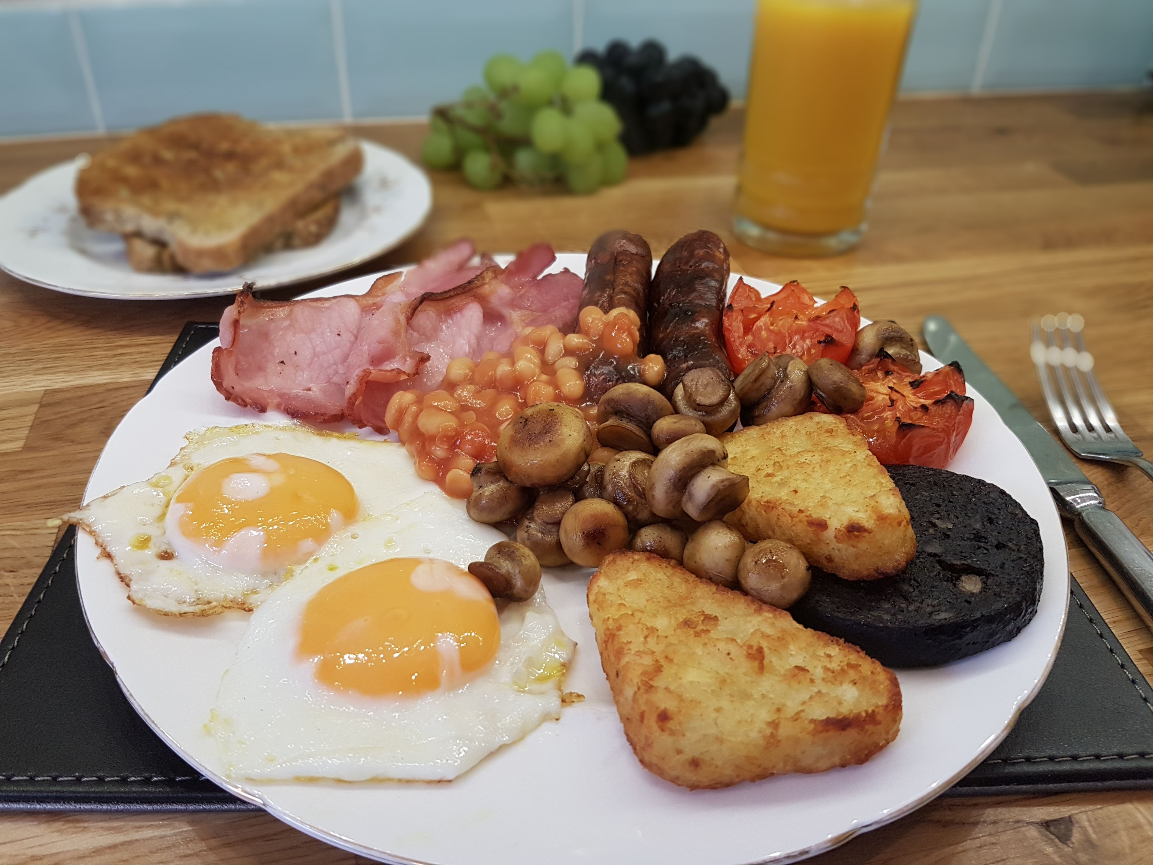 A breakfast plate with eggs, bacon, sausages, mushrooms, baked beans, roasted tomatoes, and toast.