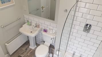 Un baño con lavamanos blanco, inodoro y bañera, suelo de madera y un espejo sobre el lavamanos.