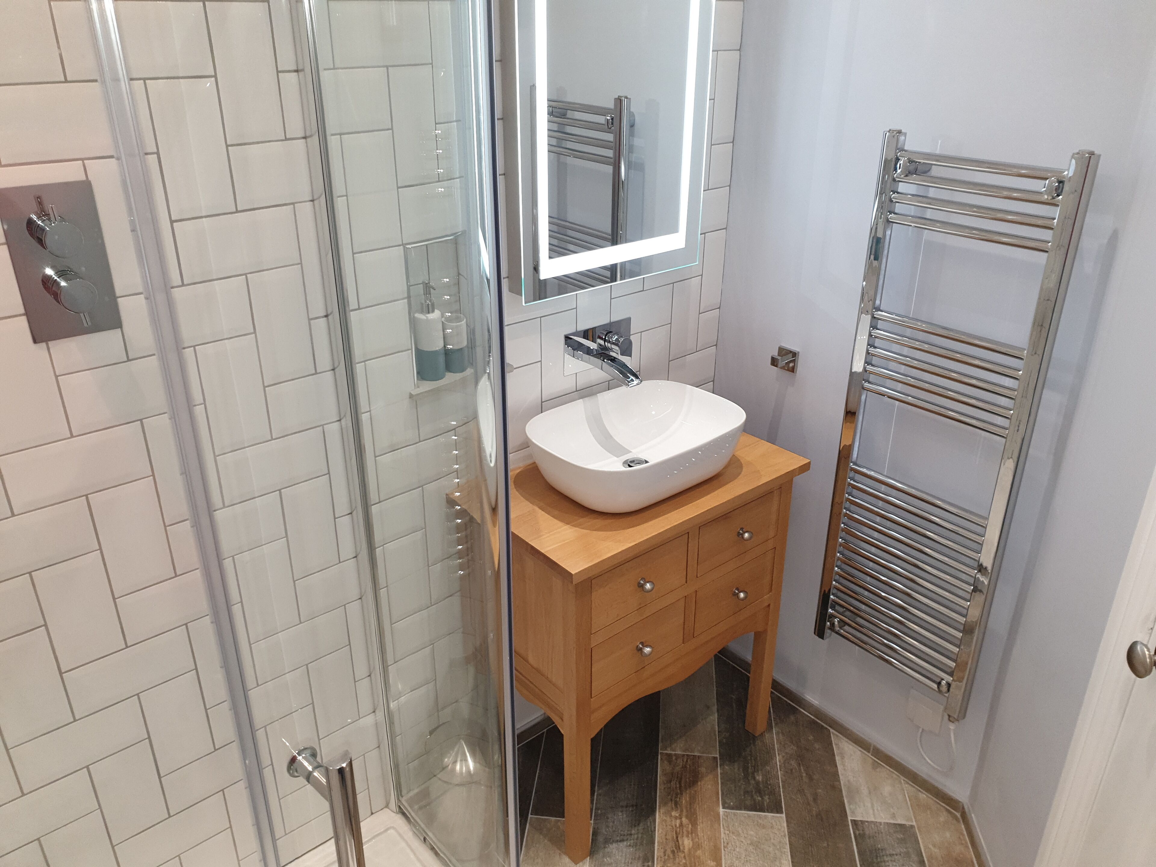Un baño con cabina de ducha de vidrio, un lavamanos blanco con espejo y un mueble de tocador de madera con cajones.