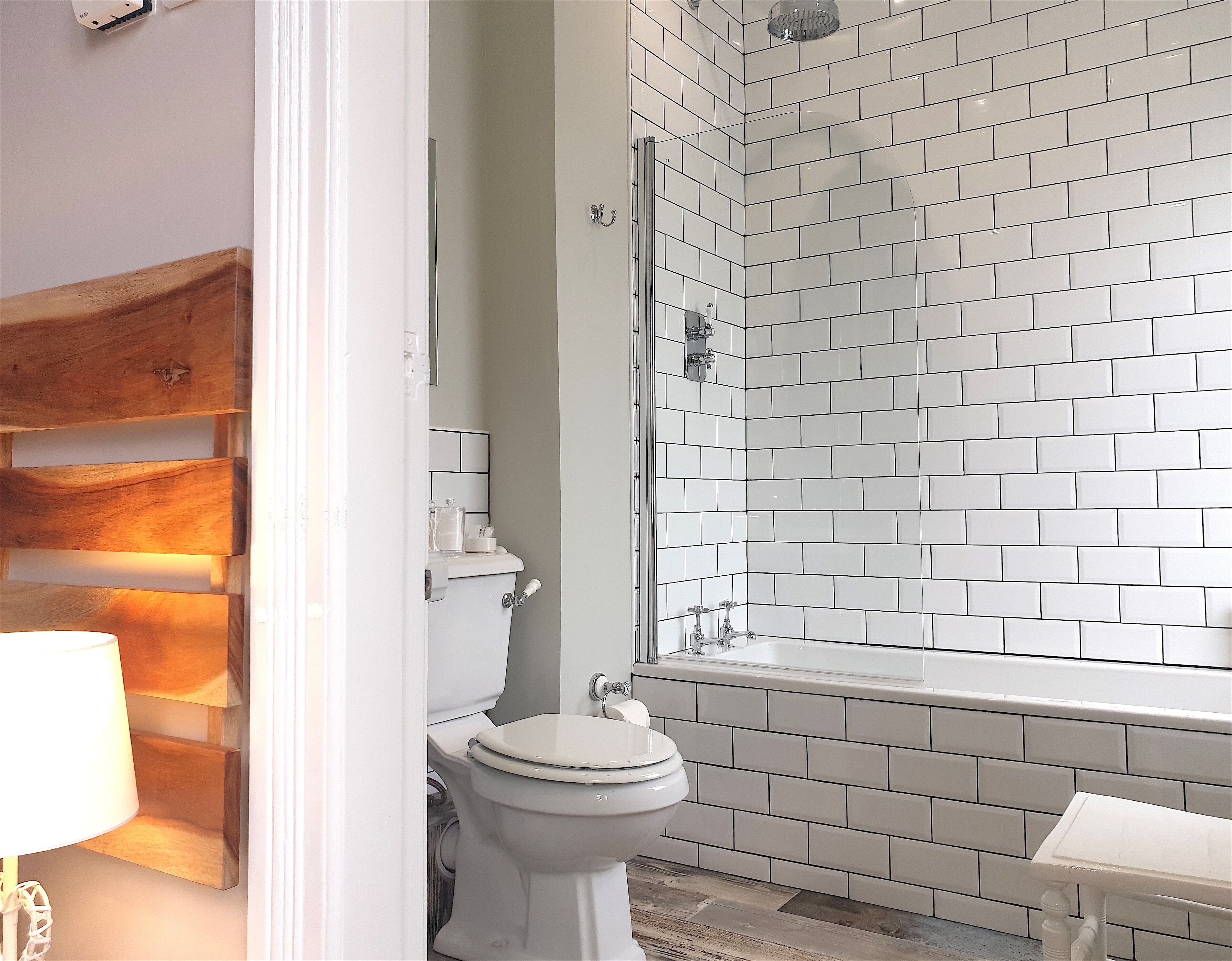 Une salle de bain avec des carreaux de céramique blancs rectangulaires, des toilettes blanches et un espace douche.