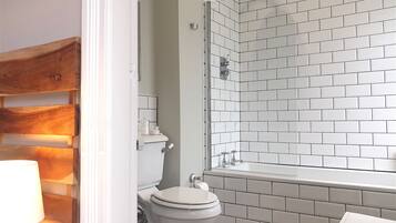 Une salle de bain avec des carreaux de céramique blancs rectangulaires, des toilettes blanches et un espace douche.