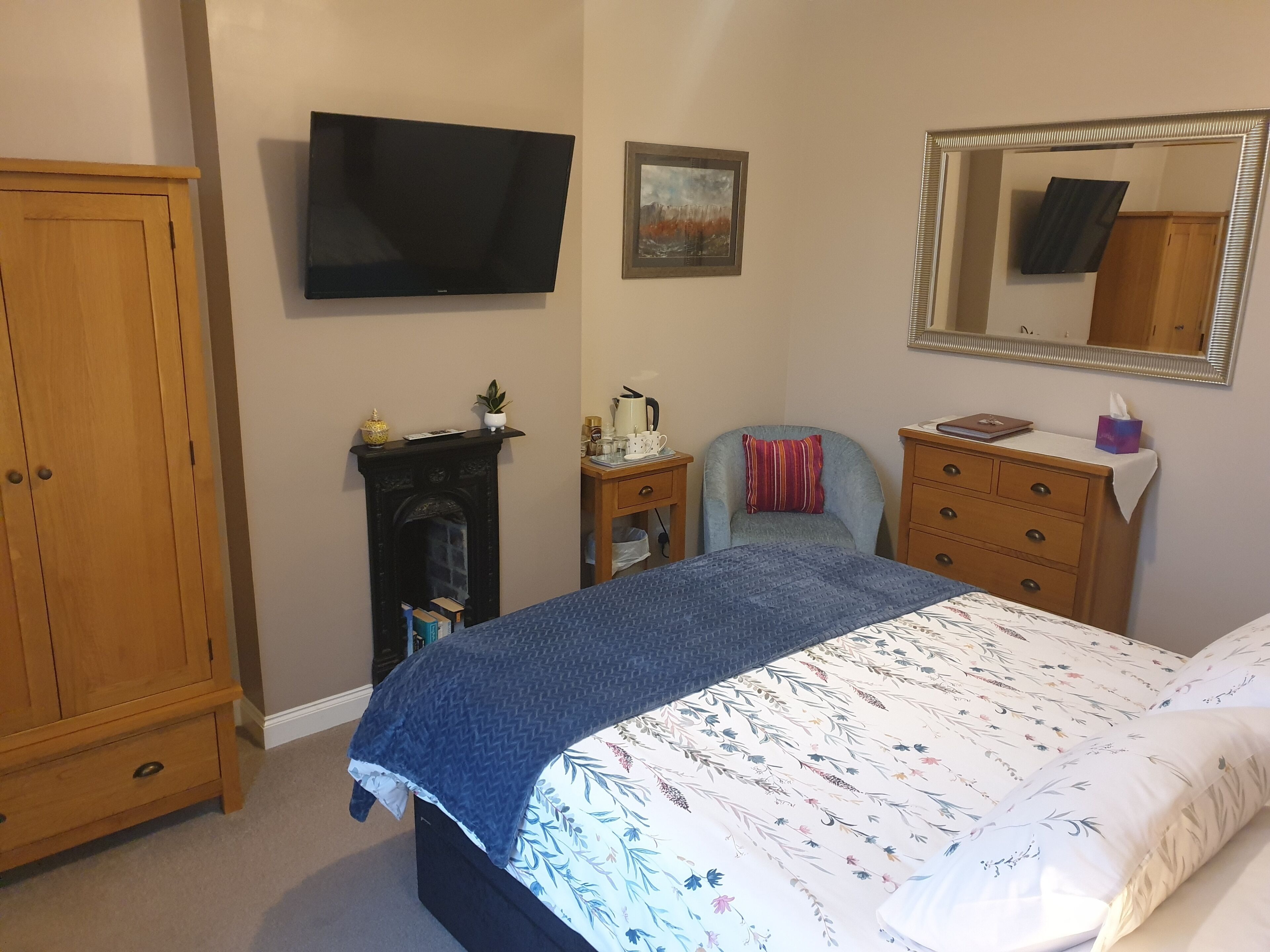 A bedroom with a bed, a dresser, a nightstand, a television, a fireplace, and a mirror.