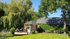 A cozy cottage with a small porch, surrounded by lush greenery and a well-maintained lawn.