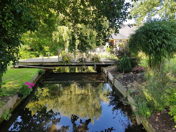 A serene garden with a small pond, a wooden bridge, and lush greenery.