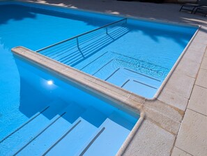 Ein Schwimmbecken mit glatter Wasseroberfläche, einer Metallleiter und einer gefliesten Umrandung.
