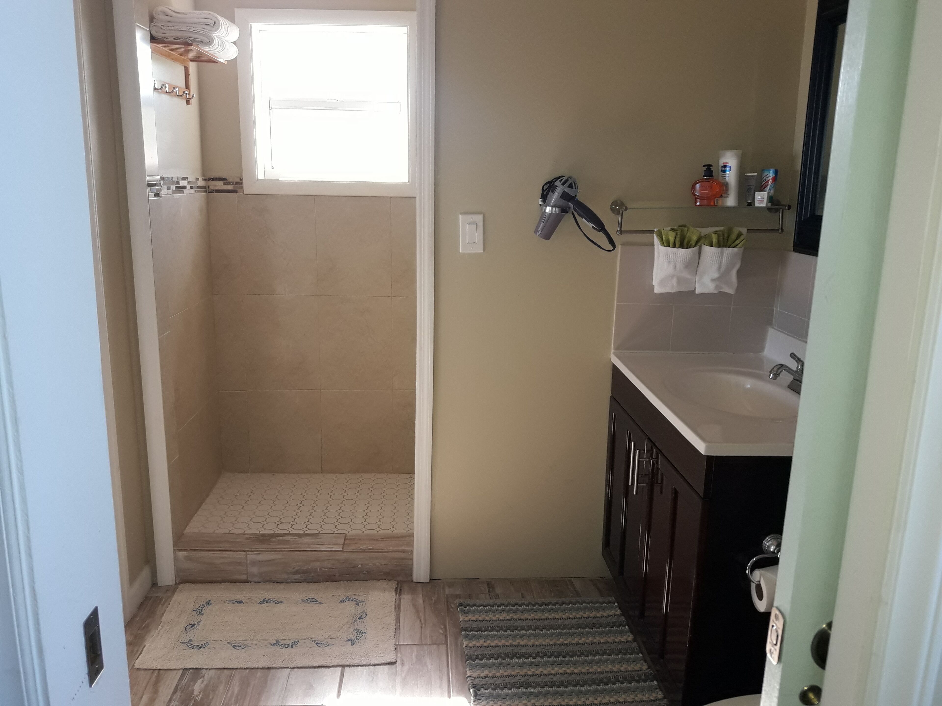 A bathroom with a shower, sink, and a small window.