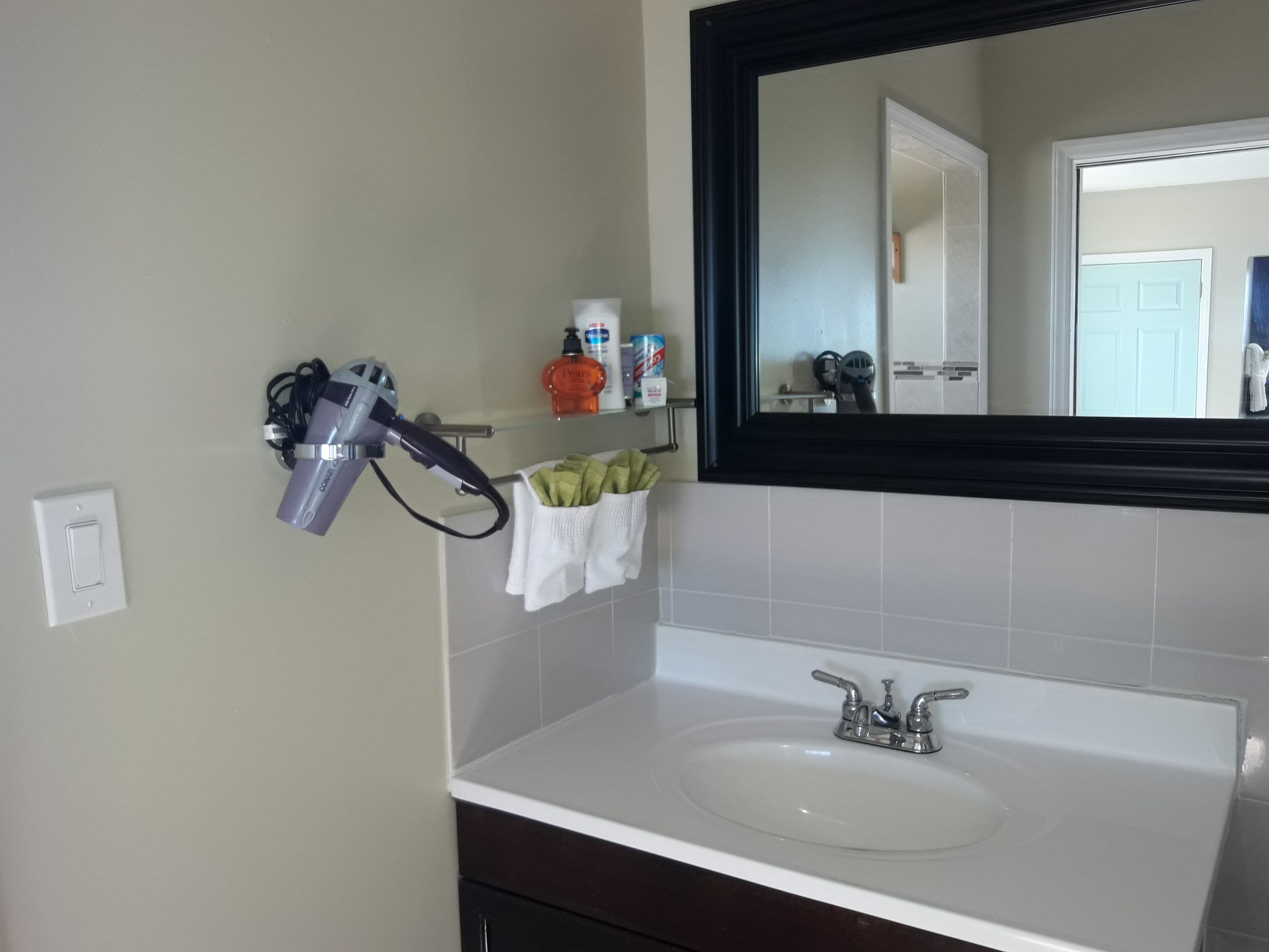 A bathroom with a white sink, a mirror, and a hairdryer on a wall-mounted rack.
