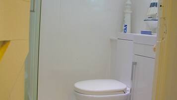 Un baño pequeño y blanco con inodoro, bañera y ventana sobre el inodoro.