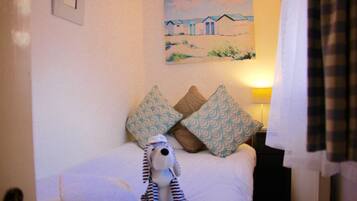A neatly made bed with patterned pillows, a small stuffed toy, and a painting of beach houses on the wall.