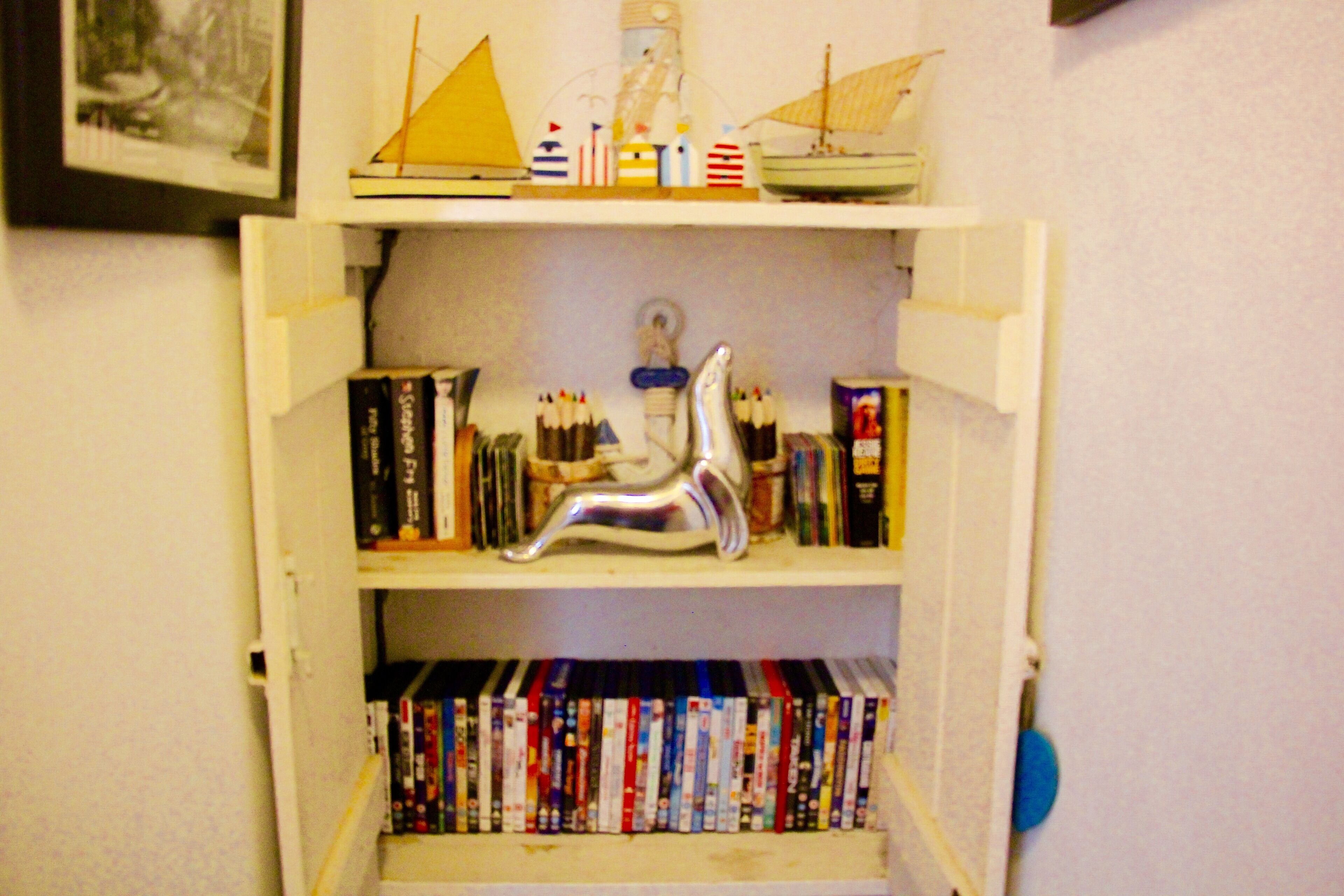 A bookshelf with various books and decorative items, including a model ship and a silver sculpture.