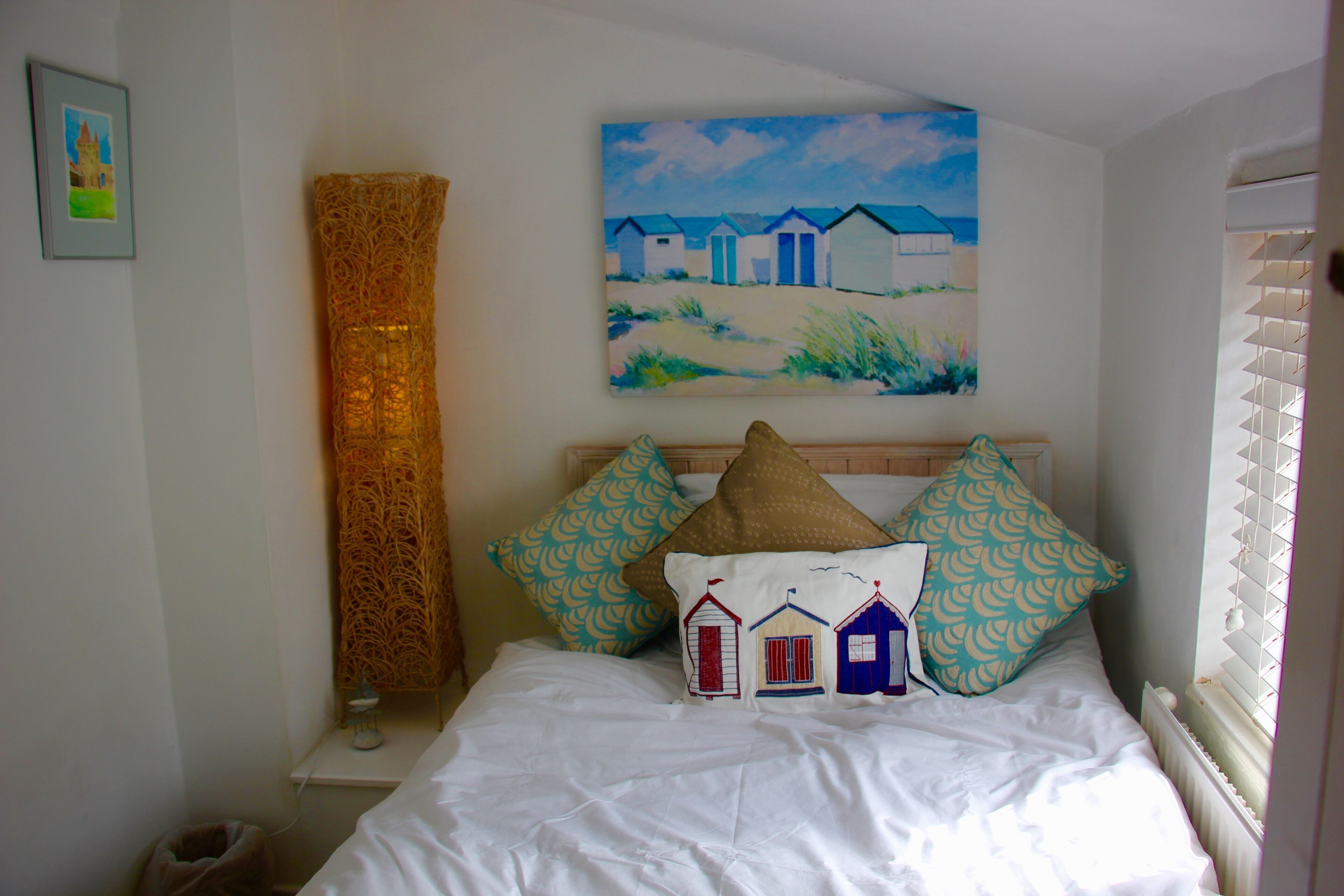 A bedroom with a bed, pillows, a painting, a lamp, and a radiator.