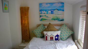 A bedroom with a bed, pillows, a painting, a lamp, and a radiator.