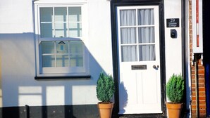 Un edificio blanco con un marco de ventana negro y una puerta. Hay dos plantas en macetas frente a la puerta.