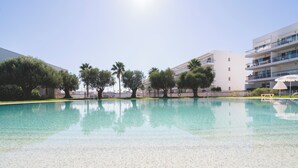 A swimming pool with clear water, surrounded by trees and modern buildings. - Marina Apartment | Poolside Balcony | Walk to Town & Beaches (Lagos)
