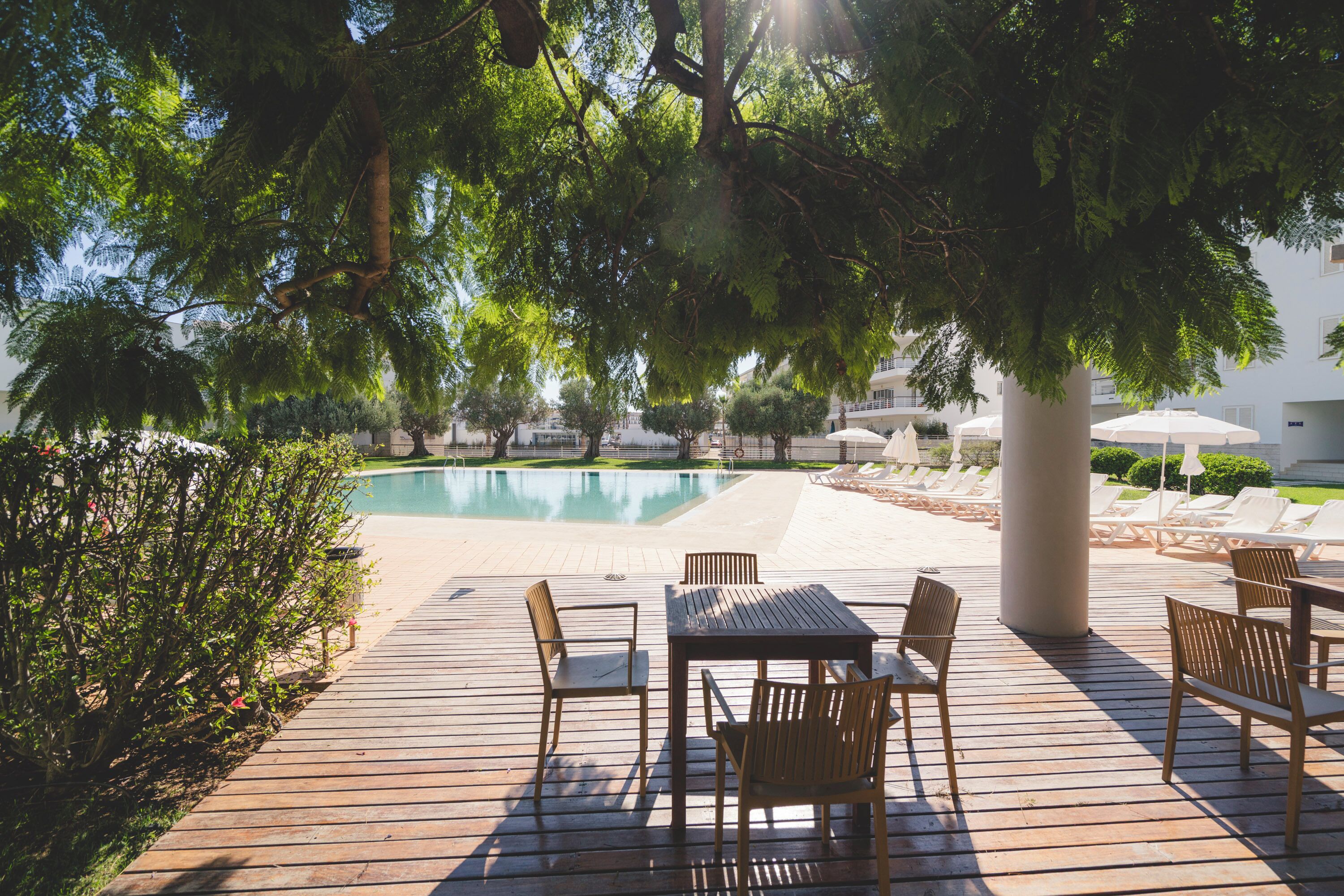 A poolside area with wooden deck, lounge chairs, and a table.