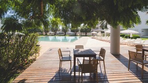 A poolside area with wooden deck, lounge chairs, and a table. - Marina Apartment | Poolside Balcony | Walk to Town & Beaches (Lagos)