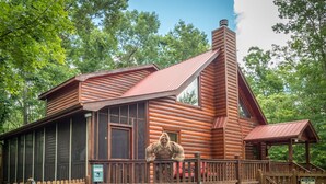 A rustic cabin with a large window, a chimney, and a fenced deck.