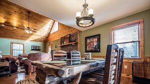 A rustic interior with a wooden dining table, leather chairs, a stone fireplace, and a chandelier.