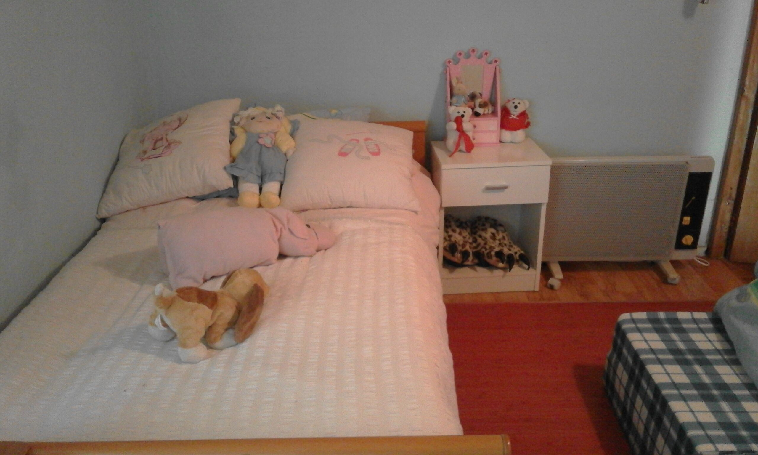 Ein Schlafzimmer mit Bett, Kissen, Stofftieren, einem Nachttisch, einer Kommode und einer Heizung.