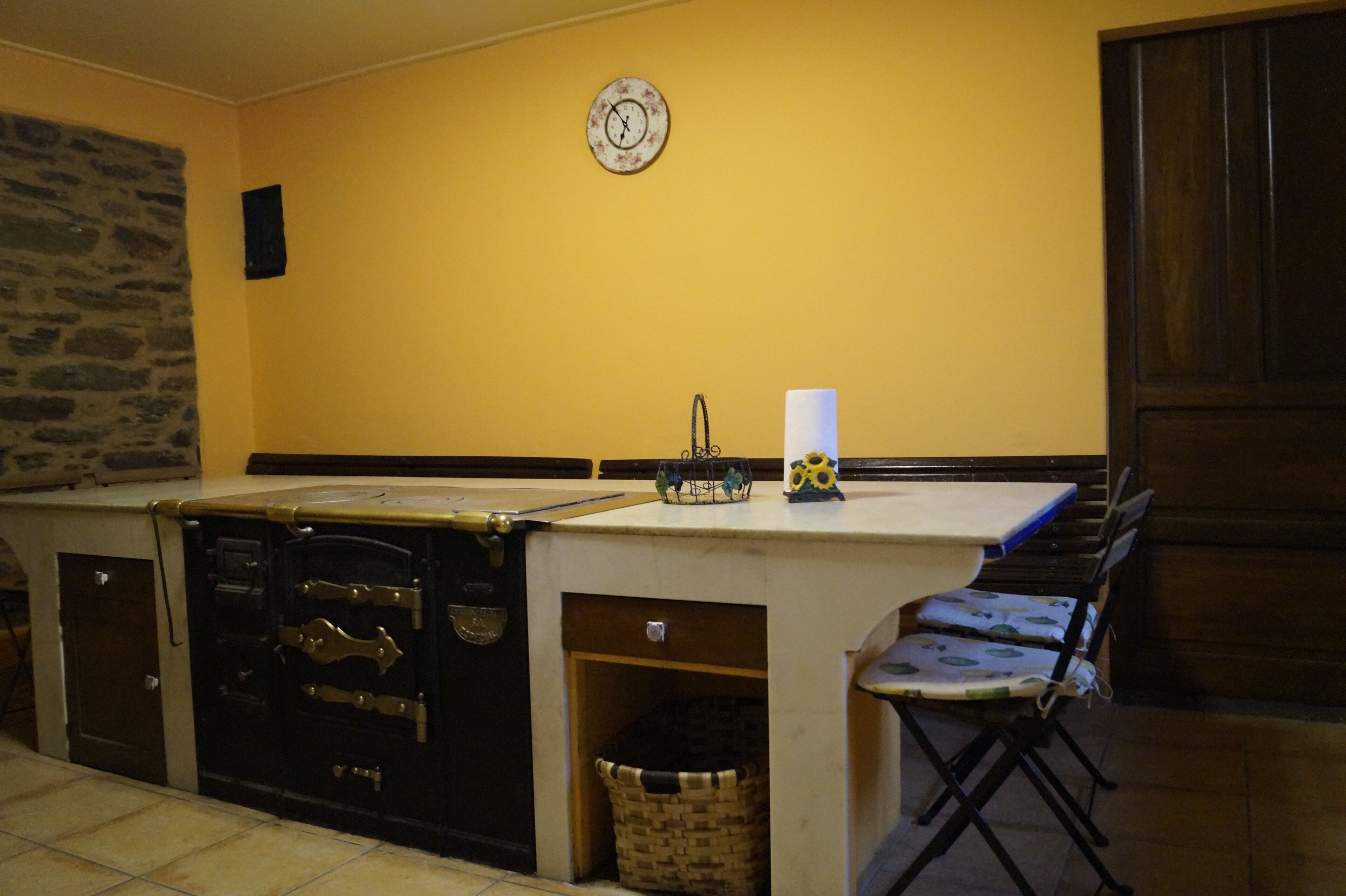 A kitchen with a stone wall, a clock, and a wooden cabinet.