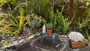 A garden with various plants, a grill, and a decorative white object.