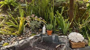 Un giardino con diverse piante, un barbecue e un oggetto decorativo bianco.